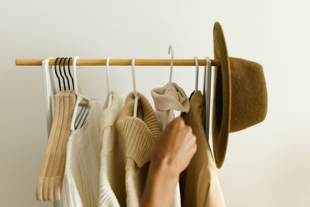 Vetements beige et brun sur un portant, une main saisit un cintre