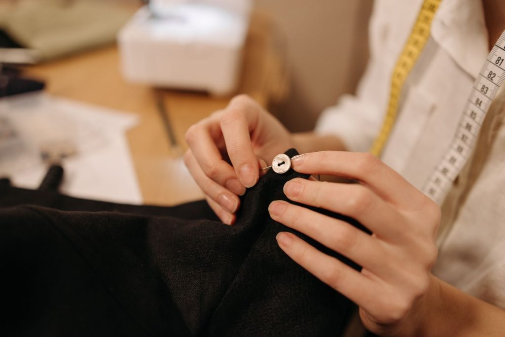 Mains d un tailleur cousant un bouton avec aiguille et fil